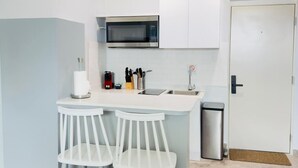 Une cuisine compacte équipée d’un four à micro-ondes, de deux tabourets de bar blancs, d’un évier et d’une poubelle.