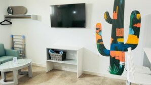 Un salon moderne doté d’un téléviseur à écran plat, d’une œuvre d’art représentant un cactus, d’un canapé, d’une table basse et d’un coin repas.
