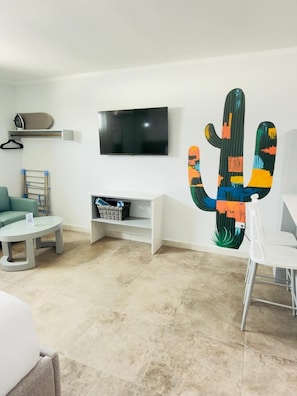 Una sala moderna con televisor de pantalla plana, una obra de arte con cactus, un sofá, una mesa de centro y un comedor.