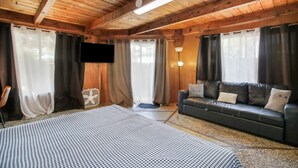 Una habitación de cabaña de madera con cama, sofá, cortinas, televisor y lámpara.