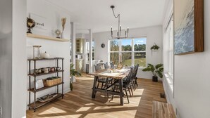 Een eetruimte met een houten tafel, stoelen en een kroonluchter. Er is een boekenkast met decoratieve objecten en een uitzicht op het buiten.