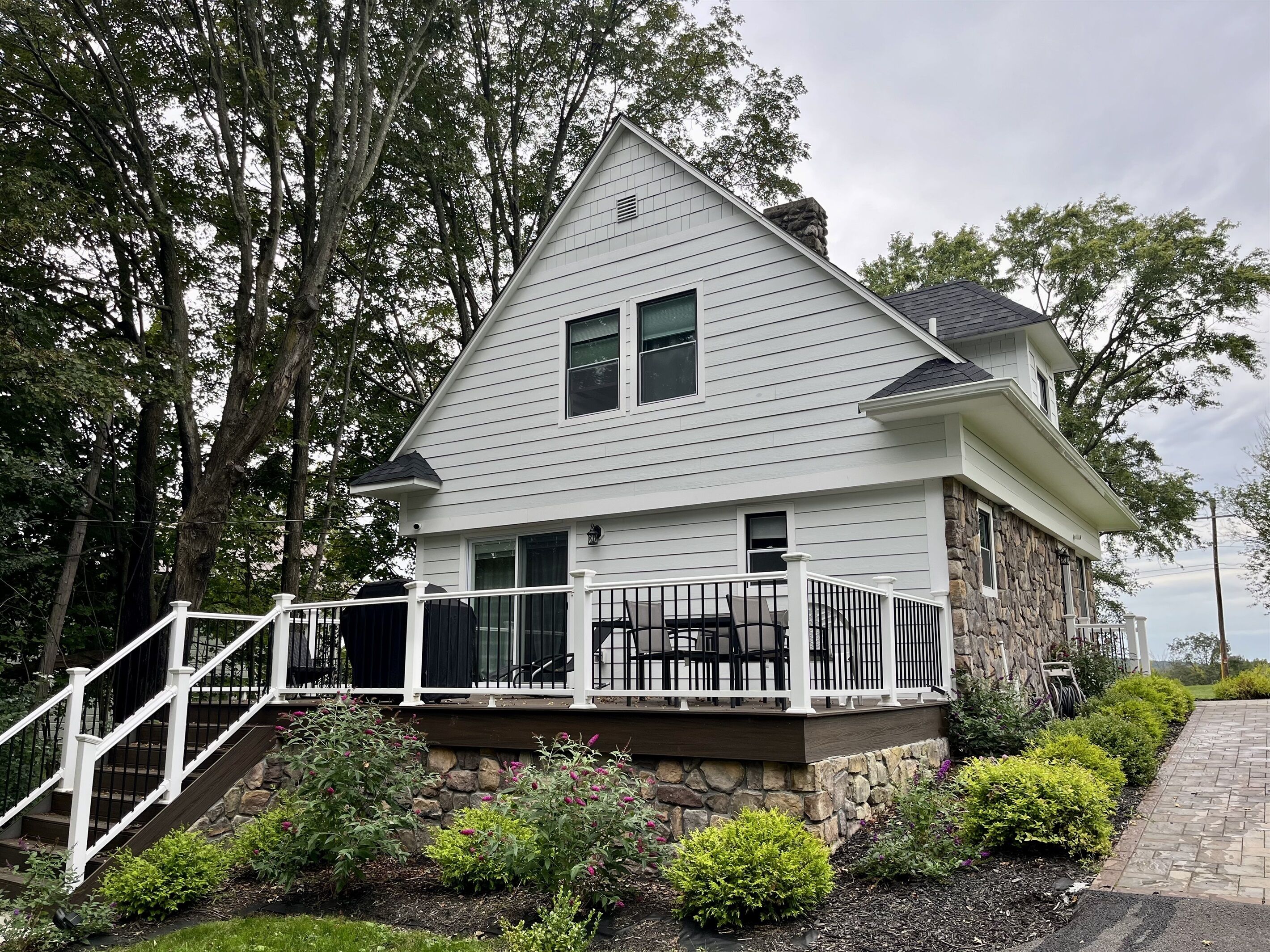 A two-story house with a stone foundation, white siding, and a covered front porch with black outdoor furniture.