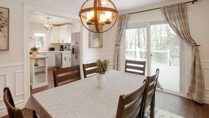 Un espace repas comprenant une table ronde, des chaises, un lustre et une vue sur la cuisine et la terrasse extérieure.