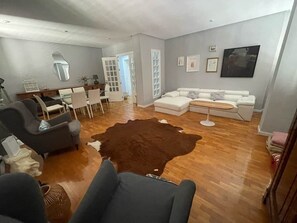 Ein Wohnzimmer mit braunem Teppich, einem weißen Sofa und einem Essbereich mit Stühlen und einem Tisch.