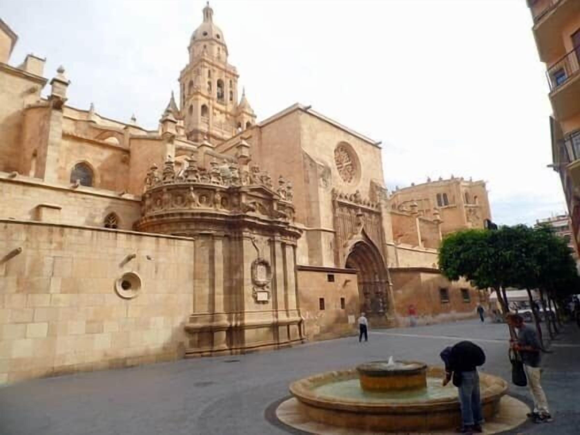 Un edificio histórico con una imponente torre de reloj, una fuente y una gran entrada en arco.