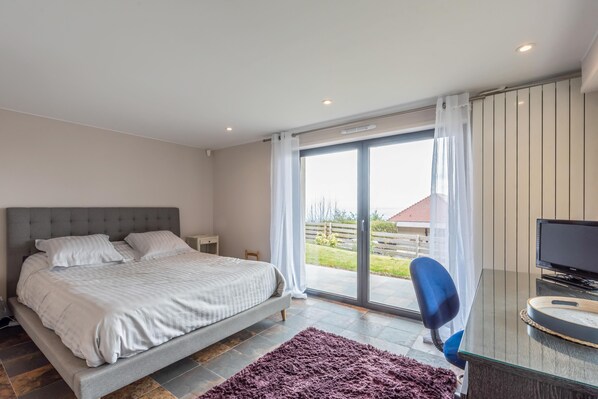 Une chambre à coucher comprenant un lit, un bureau avec une chaise et une grande porte-fenêtre coulissante donnant sur un balcon.