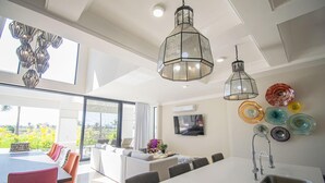 Eine moderne Küche mit einer großen Kochinsel, ein Essbereich mit langem Tisch und Stühlen sowie ein Wohnbereich mit Sofa und Fernseher.