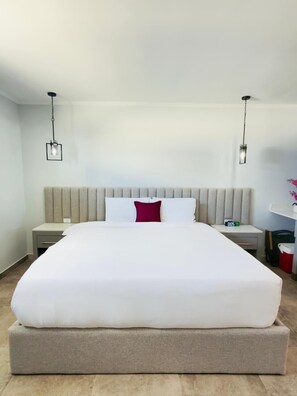 A hotel room with a large bed, two bedside tables, a nightstand, a red pillow, and a clock.