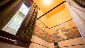 Un baño con ducha, paredes de azulejos y un ventanal con cortinas.