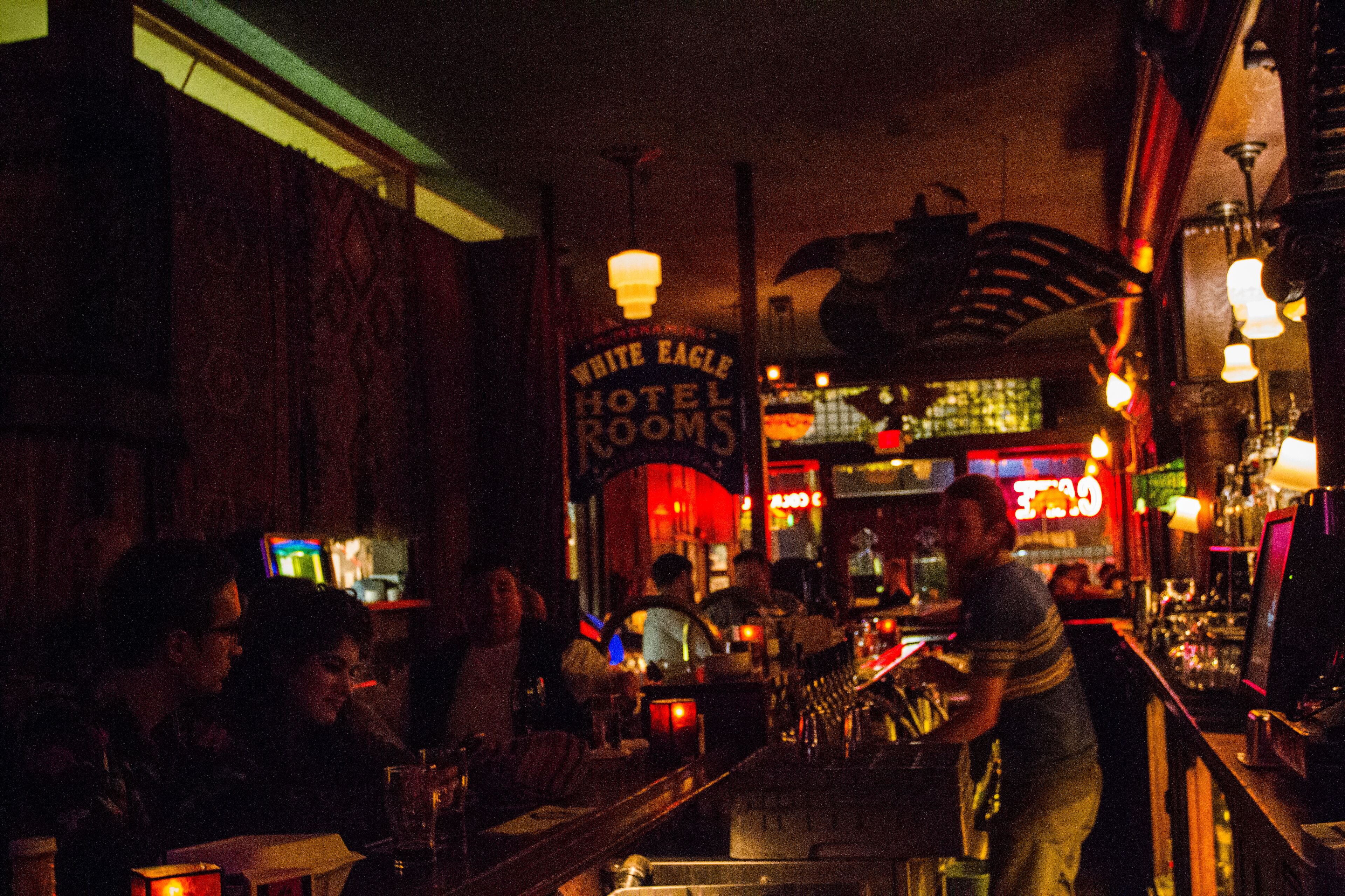 Un'area bar con un barista, tavoli e sedie. Sullo sfondo, un cartello con la scritta 'White Eagle Hotel Rooms'.