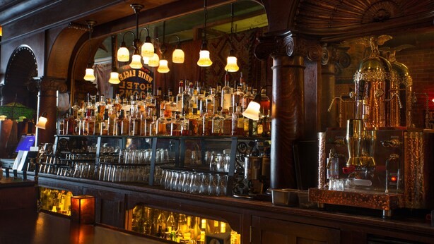 Un bar con una variedad de botellas y vasos, una máquina de café y un reloj.