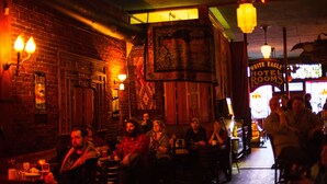Un bar tenuemente iluminado con paredes de ladrillo, faroles colgantes y un cartel que anuncia 'White Eagle Hotel Rooms'.