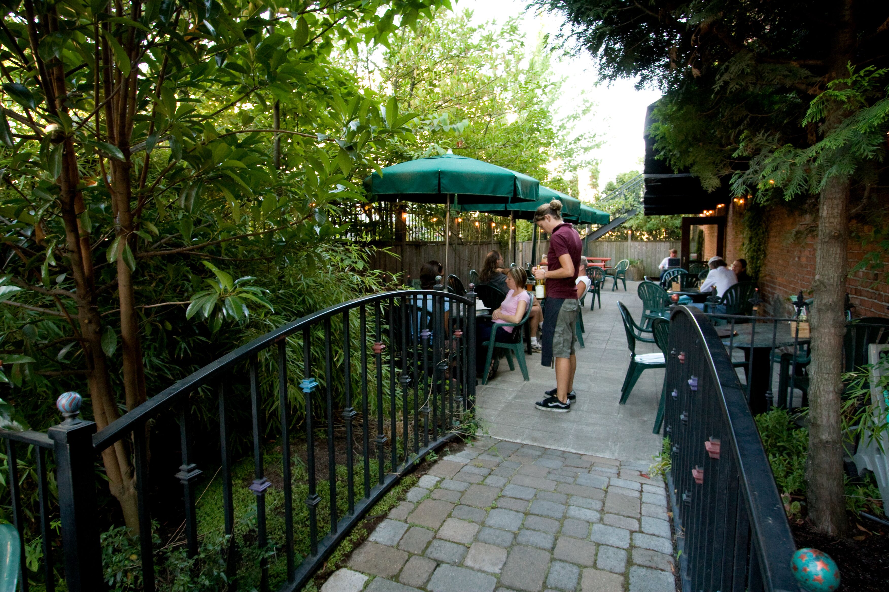 An outdoor patio area with tables and chairs, surrounded by greenery and a brick wall.