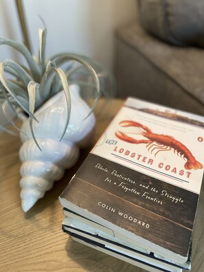 Ein Buch mit dem Titel „Die Langustenküste“ von Colin Woodard auf einer Holztischplatte.