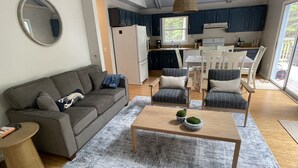 A modern living room with a grey sofa, a wooden coffee table, and a dining area with chairs and a table. - Into the Woods (Southwest Harbor)
