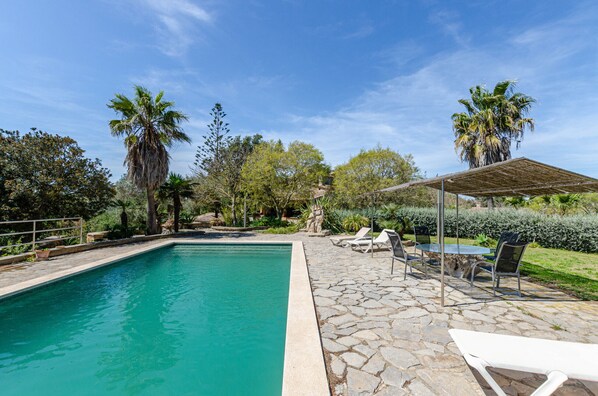 A swimming pool with lounge chairs and a covered seating area, surrounded by trees and greenery.