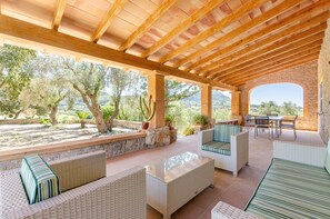 An outdoor patio with wicker furniture, a stone wall, and a view of trees and hills.
