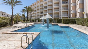 A swimming pool with a fountain, surrounded by palm trees and a multi-story building with balconies. - Golden Paradise Mar (Javea / Xàbia)