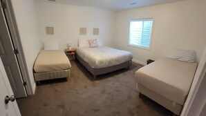 A small, well-lit bedroom with two single beds, a nightstand, a window with blinds, and a door. - Affordable Gathering Place-90 minutes to Yellowstone (Idaho Falls)