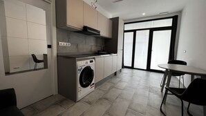 Une cuisine moderne équipée d’un lave-linge et d’un sèche-linge intégrés, un coin repas avec une table et des chaises, et une grande fenêtre qui laisse entrer la lumière naturelle.