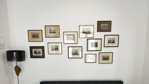 Un salon avec un canapé gris foncé, une petite table ronde surmontée d’une lampe, et un mur décoré de tableaux encadrés.