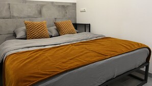 Une chambre à coucher moderne avec une tête de lit grise, un lit avec une literie grise et moutarde, et une petite table de chevet.
