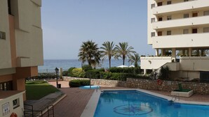 A swimming pool with a star design, surrounded by a stone wall and palm trees, with a view of the sea and a building with balconies. - Neptuno 403. Wonderful One-Bedrooms Apartment with Sea Views (Marbella)