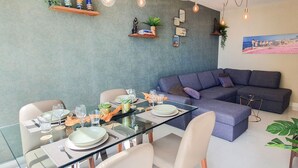A modern dining area with a glass table set for four, a grey sofa, and decorative items on the wall. - Neptuno 403. Wonderful One-Bedrooms Apartment with Sea Views (Marbella)