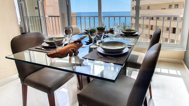 A dining area with a glass table and chairs, a decorative pig sculpture, and a view of the sea through large windows. - Neptuno 403. Wonderful One-Bedrooms Apartment with Sea Views (Marbella)
