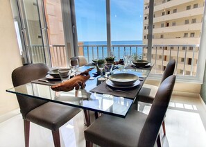 Un coin repas avec une table et des chaises en verre, une sculpture de cochon décorative et une vue sur la mer grâce à de grandes fenêtres.