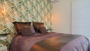 A bedroom with a bed, pillows, a wall with a leaf pattern, and a shelf with a plant. - Neptuno 403. Wonderful One-Bedrooms Apartment with Sea Views (Marbella)