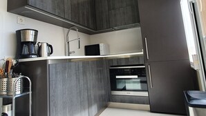 A compact kitchen with dark cabinetry, a built-in oven, a coffee maker, and a microwave. - Neptuno 403. Wonderful One-Bedrooms Apartment with Sea Views (Marbella)