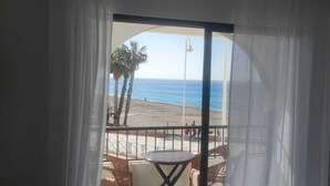 Un balcón con mobiliario de mimbre y una mesa, con vista a una playa con palmeras y el océano.