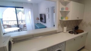 Una cocina compacta con lavadora, un lavamanos y una pequeña zona de comedor con mesa y sillas.