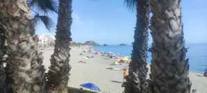 Een strand met palmbomen, parasols en mensen die ontspannen.