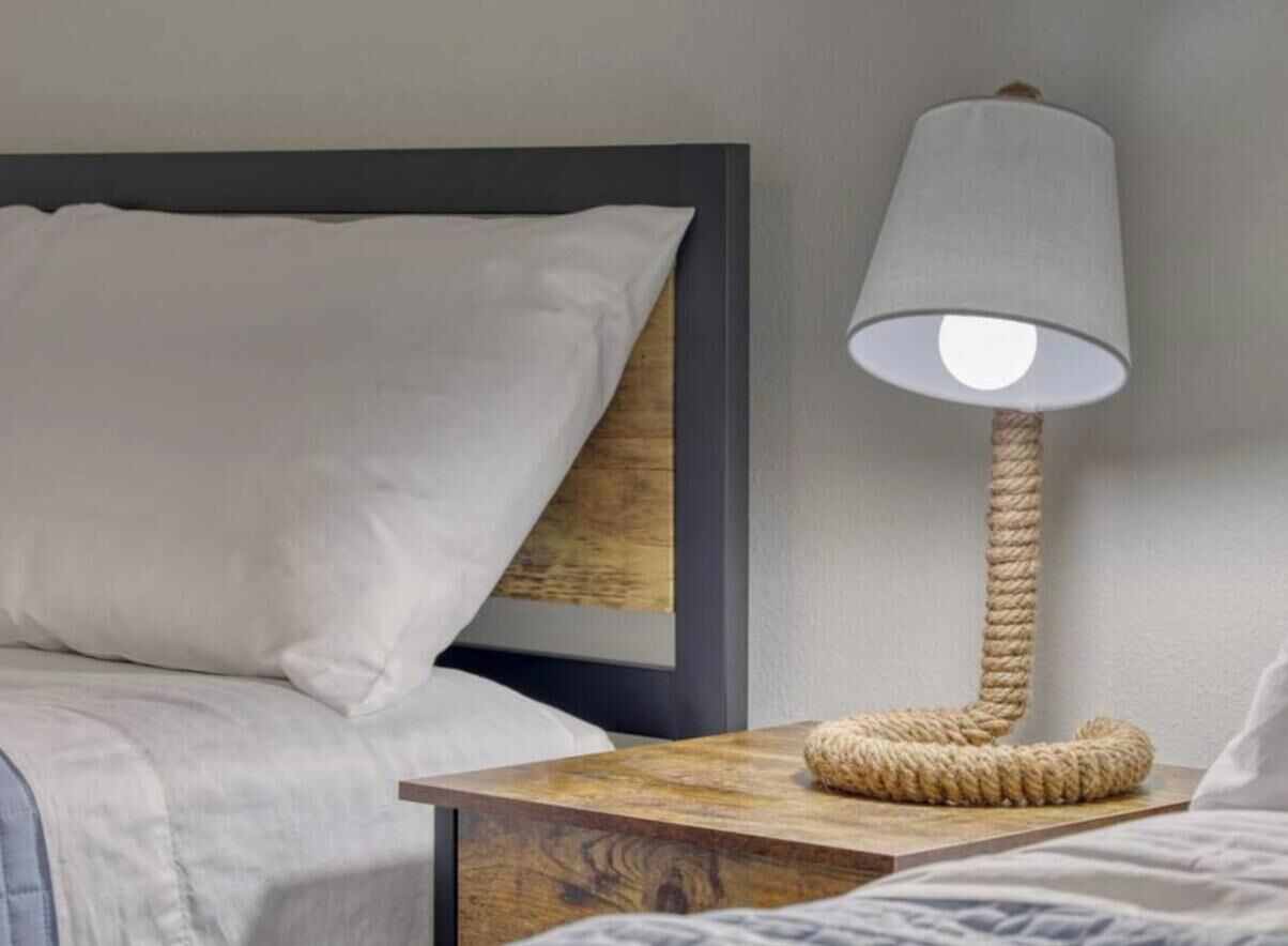 Een bed met hoofdbord, een bedlamp met een touwvoet en een houten nachtkastje.