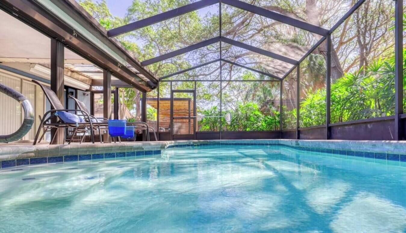 A swimming pool with a metal roof structure, surrounded by greenery.