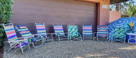 A row of beach chairs with colorful striped cushions in front of a garage door.