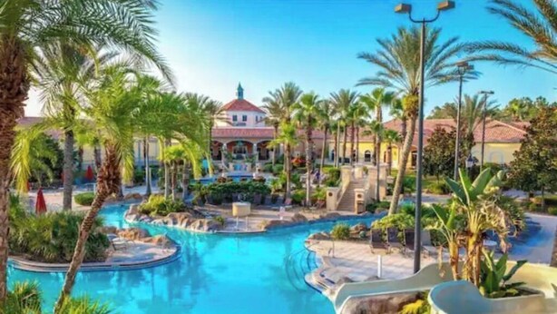 A resort pool area with palm trees, a water slide, and a building with a red roof. - Regal Palms Resort Oasis (Davenport)