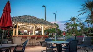 An outdoor restaurant with a thatched roof, tables, and chairs. - Regal Palms Resort Oasis (Davenport)