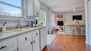 A modern kitchen with white cabinets, a double sink, and a dining area with a wooden table and chairs. - The Retreat - Private Pool-Spa-Firepit-Gameroom (Greenwood)