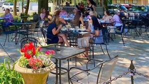 An outdoor cafe with tables and chairs arranged on a paved area, surrounded by potted plants and a building in the background. - The Retreat - Private Pool-Spa-Firepit-Gameroom (Greenwood)