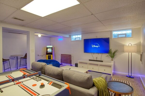 A room with a foosball table, a flat-screen TV, a sofa, and a small table with chairs. - The Retreat - Private Pool-Spa-Firepit-Gameroom (Greenwood)