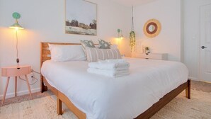 A bedroom with a wooden bed, white bedding, a bedside table, a lamp, a wall-mounted mirror, and a framed picture. - The Retreat - Private Pool-Spa-Firepit-Gameroom (Greenwood)