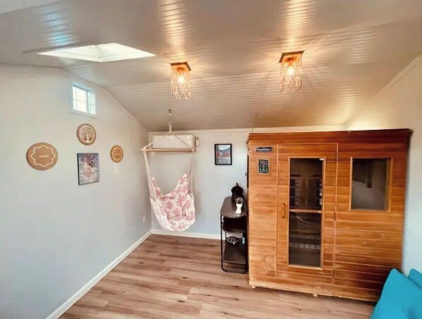 Una habitación con sauna de madera, una silla colgante y un pequeño estante con calefactor.