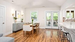 Una cocina amplia con piso de madera, un comedor con mesa y sillas, y vistas a una terraza exterior a través de puertas de vidrio.