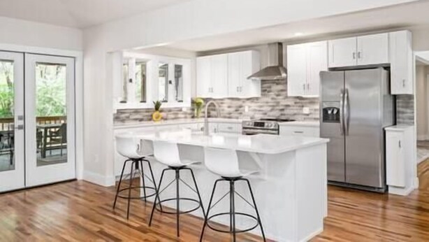 Una cocina moderna con armarios blancos, una isla grande con taburetes y un refrigerador de acero inoxidable.