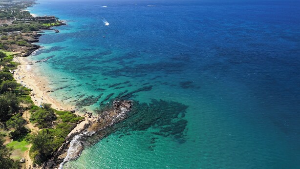 An aerial view of a coastal area with a beach, clear blue waters, and a rocky shoreline. - Maui Sunset A303 - Great large 1 bedroom close to ocean (Kihei)
