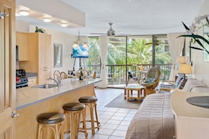 Relax in a spacious room with a comfortable sofa, dining table, and kitchen area, plus a balcony with a view of lush greenery.