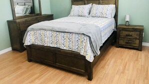 Quarto com cama de madeira, mesa de cabeceira com gavetas, espelho e abajur.